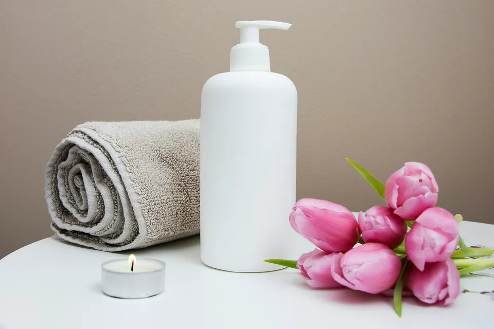 White pump bottle beside a folded towel, candle and tulips — a calm everyday beauty ritual